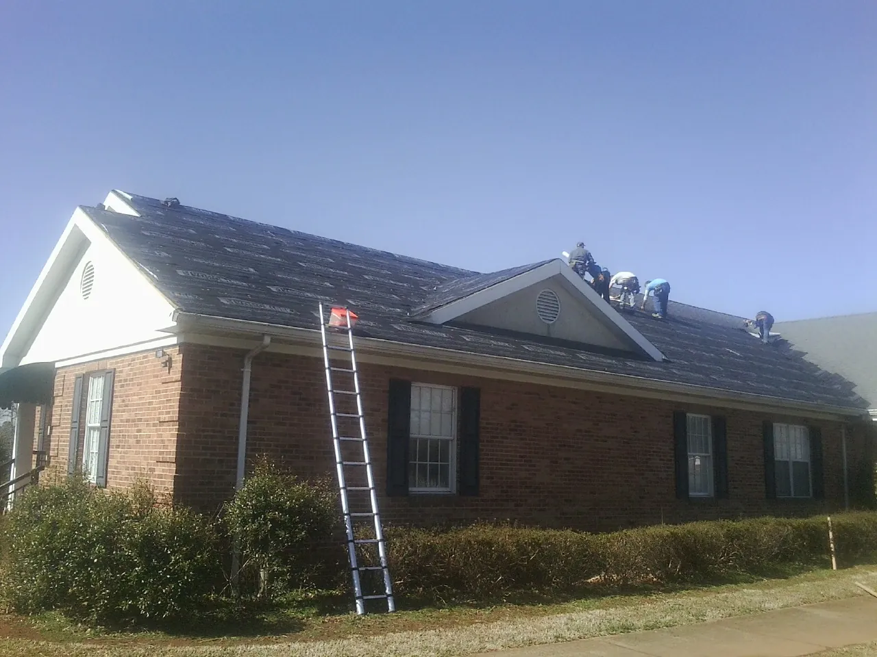 Crew tearing shingles off a brick ranch roof with a ladder set — Metal Roof Repair work by our crew in Mc Henry