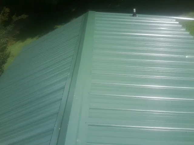 New green metal panels meeting at the ridge of a roof — Flat Roof Repair work by our crew in Mc Henry