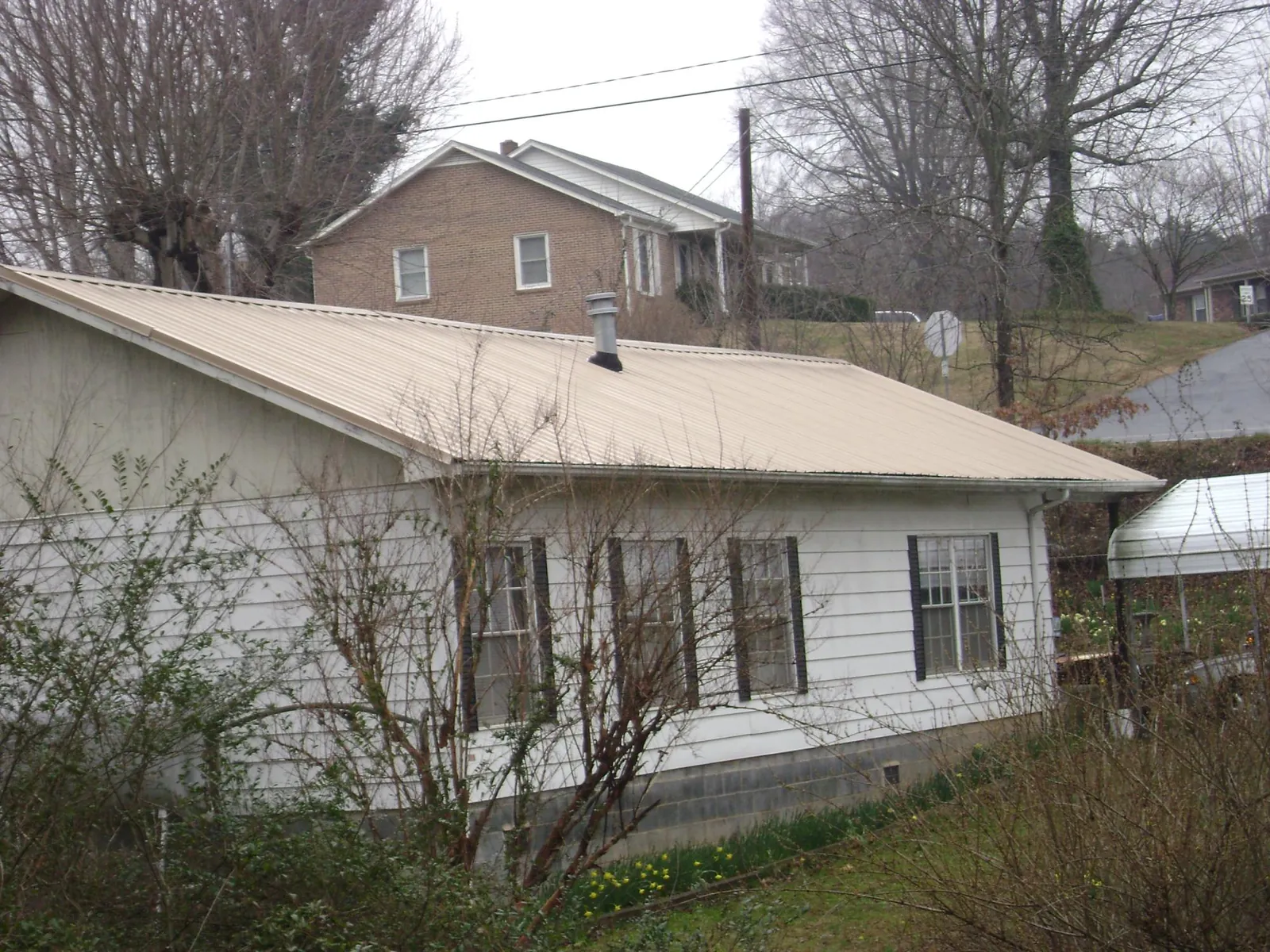 Tan metal roof on a white sided house set into a hillside — Commercial Roofing by Roofing Brothers in Mc Henry