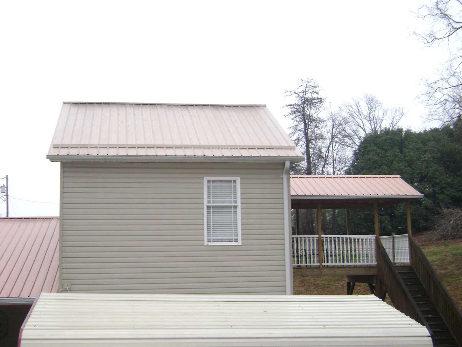 Tan metal roofs on a two story addition and attached porch, from a Roof Replacement job in Mc Henry